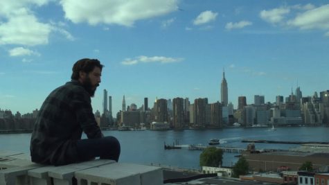 Frank Castle, The Punisher, sits on the edge of a rooftop and eats a sandwich.